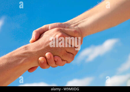 Two male hands, handshake close up on diagonal against and the blue sky. Stock Photo