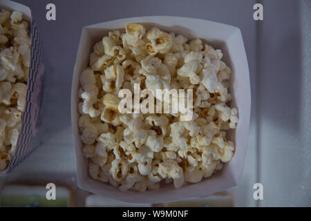 A wide classic box of theater popcorn isolated on white . Popcorn spilled from a striped box . Three vintage-style boxes of popcorn in a carnival them Stock Photo