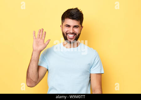 Hello Hi Young cheerful handsome bearded man greeting with open hand, enjoying communication, isolated on yellow background. close up portrait, body l Stock Photo