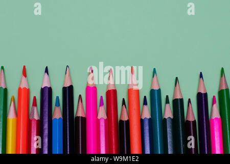 Many colored pencils lie on a green background. Copy spase. The concept of back to school, the educational process, study at school, drawing. Stock Photo