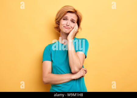 unhappy blonde woman having a toothache, tooth decay, girl suffering from pain in tooth, woman has a problem with health, isolated yellow background, Stock Photo
