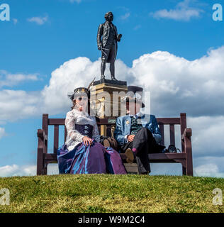 Steampunk couple sat on bench below Captain Cook memorial, Whitby, UK. Stock Photo