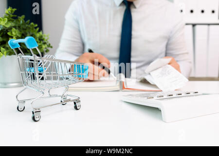Businessman calculating shopping expenses, holding receipts in hand. Empty shopping cart in front. Home finances, investment, economy, saving money co