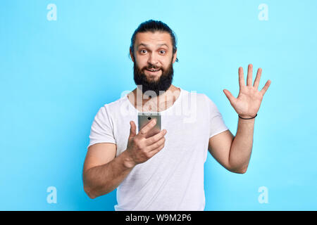 happy emotional positive man using mobile phone.standing isolated over blue background. man greeting somebody, internet connection Stock Photo