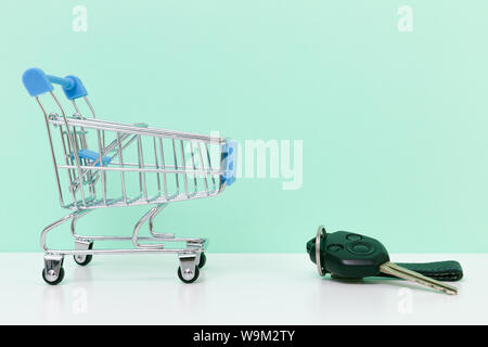 Car purchase concept. Empty shopping cart and car keys on white table with light blue background Stock Photo