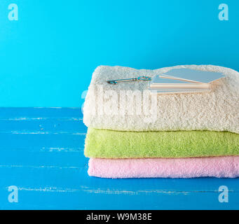 three multi-colored new terry bath towels folded on a blue wooden background and empty paper business cards Stock Photo