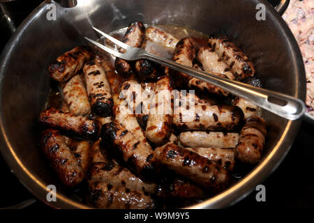 Tasty sausages being cooked on a BBQ by a chef and served up in a pan. Delicious! Stock Photo