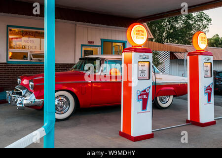 Dusk view of 1955 Studebaker President classic car parked in front of antique gas pumps converted to electric car chargers; The Circle R Motel; Salida Stock Photo