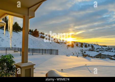 View from a covered deck as the setting sun illuminates a large icicle on a snow covered hill above a neighborhood subdivision in Spokane Washington Stock Photo