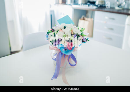 Bouquet of flowers with card in gift box left on kitchen table. Surprise for woman. Present for holiday Stock Photo