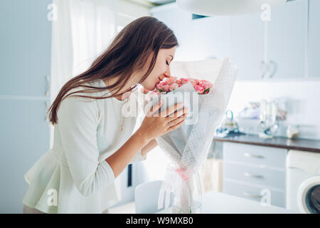 Happy woman smelling bouquet of roses. Housewife enjoying decor and interior of kitchen. Sweet home. Allergy free Stock Photo