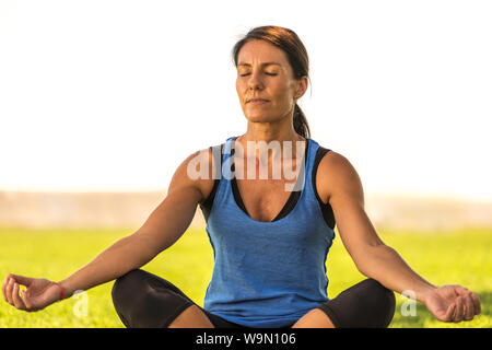 Young caucasian woman stretches, meditates, and gets focussed in the grass outside in a park setting Stock Photo