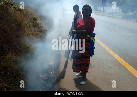 Two ladies burning leaves and rubbish in roadside ditch, Lilongwe, Malawi, Africa. Stock Photo