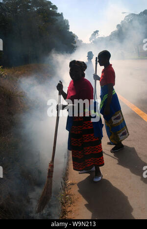 Two ladies burning leaves and rubbish in roadside ditch, Lilongwe, Malawi, Africa. Stock Photo