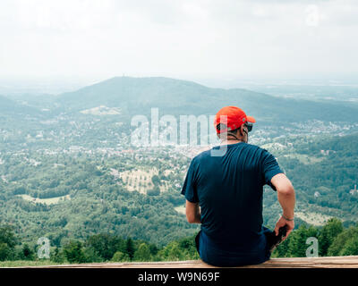 Baden-Baden, Germany - Jul 7, 2019: Rear view of senior man taking smartphone from his pocket on top of the mountain with Baden-Baden city in the valley Merkurweg Stock Photo