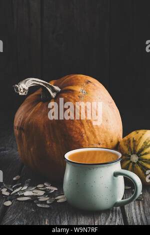 Cup of fresh pumpkin juice, ripe pumpkins and seeds on wooden table. Stock Photo