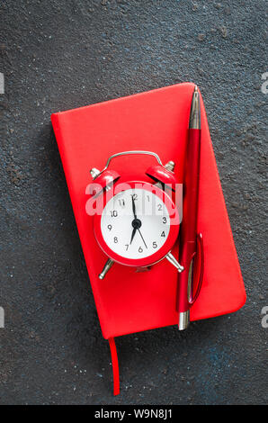 Alarm clock, notepad and pen on dark background. Concept time management or education. Copy space. Stock Photo
