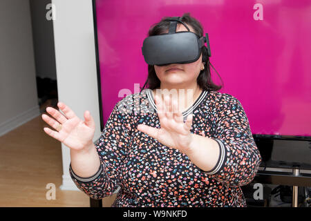 Woman in front of a television screen with blank space is playing a game using virtual reality headset Stock Photo