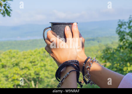 Hands with a mug on the background of a mountain landscape. Womans is holding cup of tea the outdoors. Stock Photo