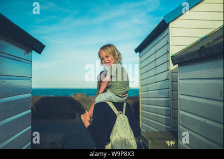 A little toddler is riding on his mother's shoulders by the sea Stock Photo