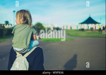 A little toddler is riding on his mother's shoulders at sunset in the park Stock Photo
