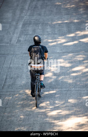 Cyclist in black clothes with a backpack rides a bicycle on a footpath. The use of a bicycle as the main transport for many enthusiasts has grown from Stock Photo