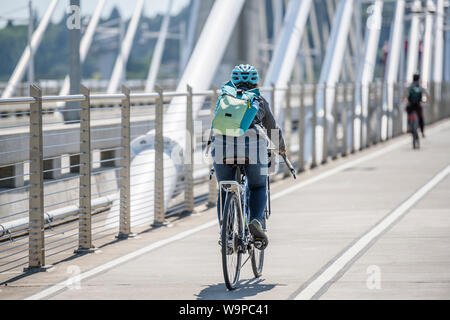 A gorgeous woman cyclist in sportswear and helmet crosses the crossroad on a bicycle, preferring an active way of relaxation, helping her to keep hers Stock Photo