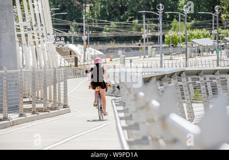 A gorgeous woman cyclist in sportswear and helmet crosses the crossroad on a bicycle, preferring an active way of relaxation, helping her to keep hers Stock Photo