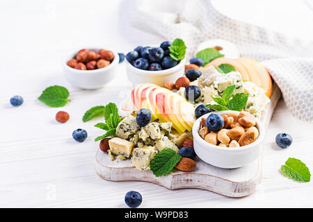 Cheese platter with assorted cheeses, blueberry, apples, nuts on white table. Italian cheese  platter and fruit. Stock Photo