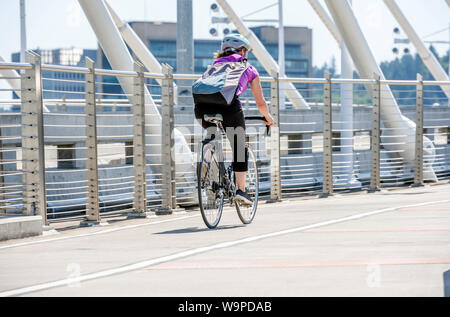 A gorgeous woman cyclist in sportswear and helmet crosses the crossroad on a bicycle, preferring an active way of relaxation, helping her to keep hers Stock Photo