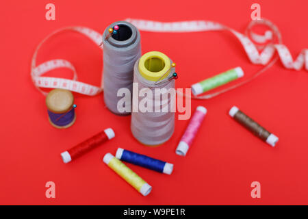 Composition with threads and sewing accessories on a red background. Sewing supplies and needlework accessories. Spools of thread, scissors and needle Stock Photo
