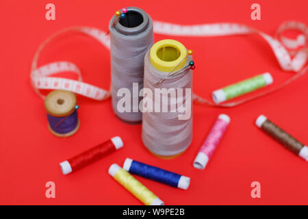 Composition with threads and sewing accessories on a red background. Sewing supplies and needlework accessories. Spools of thread, scissors and needle Stock Photo