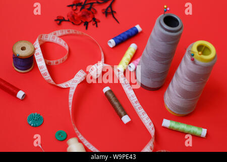 Composition with threads and sewing accessories on a red background. Sewing supplies and needlework accessories. Spools of thread, scissors and needle Stock Photo
