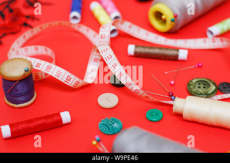Composition with threads and sewing accessories on a red background. Sewing supplies and needlework accessories. Spools of thread, scissors and needle Stock Photo