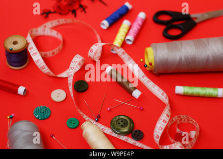 Composition with threads and sewing accessories on a red background. Sewing supplies and needlework accessories. Spools of thread, scissors and needle Stock Photo