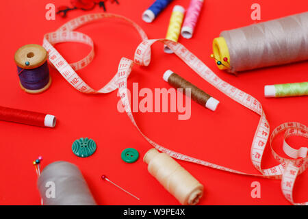 Composition with threads and sewing accessories on a red background. Sewing supplies and needlework accessories. Spools of thread, scissors and needle Stock Photo