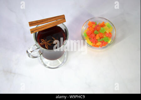 A glass cup of mulled wine with cinnamon sticks and star anise flowers, next to a cup of dried fruit. Stock Photo