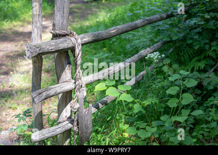 Knot bound wooden stick fence on a background of green grass. rope tied of old fence. Stock Photo