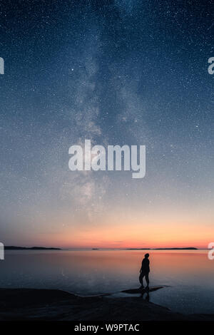 A man standing by a calm sea and looking up on the stars of the milky way Stock Photo