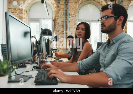 Working together. Two young business people working on computers and discussing new project while sitting at desk in modern open space. Job concept. Workplace. Teamwork Stock Photo
