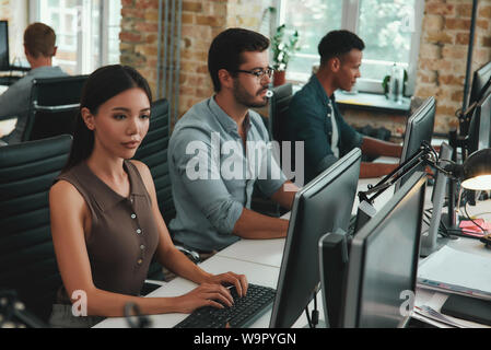 Daily routine. Group of young employees working on computers while sitting in modern open space. Job concept. Business people. Workplace Stock Photo