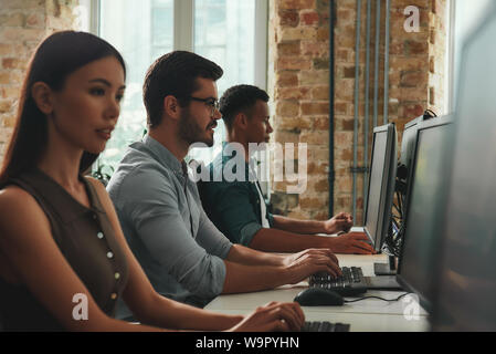 Office life. Side view of young employees working on computers while sitting in modern open space. Job concept. Business people. Workplace Stock Photo
