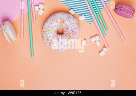 Crwative composition with sweet treats and party decor. Donuts, macarons, marshmallows and paper straws on pastel background