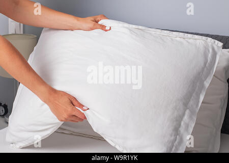 Woman's hands close-up making the bed. Housekeeper changing the linen and putting pillows on the bed with fresh clean white bedding. Stock Photo