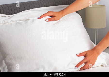 Woman's hands close-up making the bed. Housekeeper changing the linen and putting pillows on the bed with fresh clean white bedding. Stock Photo