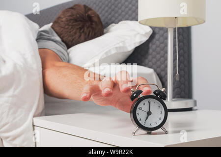 Man's hand reaching out alarm clock on the nightstand early in the morning. Morning routine. Stock Photo