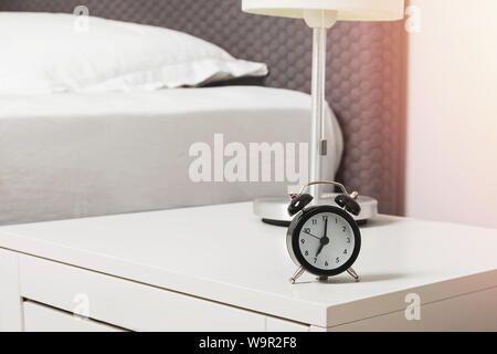 Alarm clock standing on the nightstand near the bed close-up Stock Photo