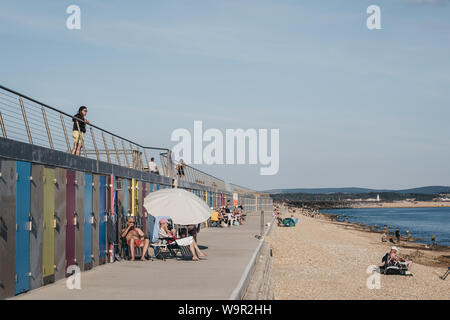 Milford on Sea, UK - July 13, 2019: People relax by new beach huts in Milford on Sea, UK. Opened in May 2017, they replaced 119 concrete huts which we Stock Photo