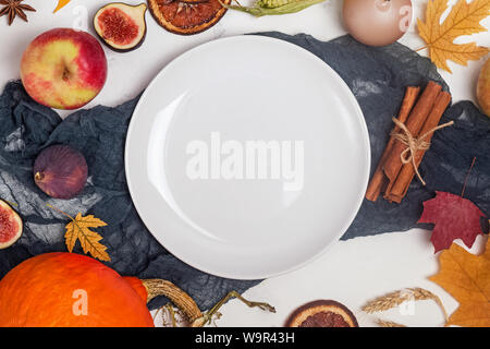 Thanksgiving day table setting with white plate and different fruits, spices and yellow leaves Stock Photo