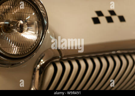 fragment of the front part of a vintage taxi car, focus on the headlight, checker emblem and radiator in blur Stock Photo